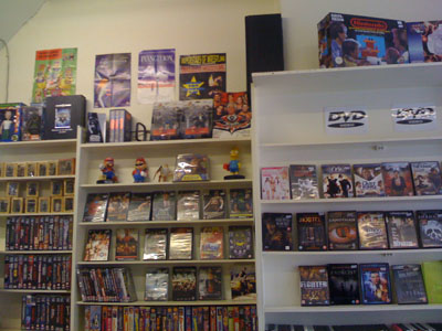 DVDs and collectibles on shop shelves with console boxes on top.